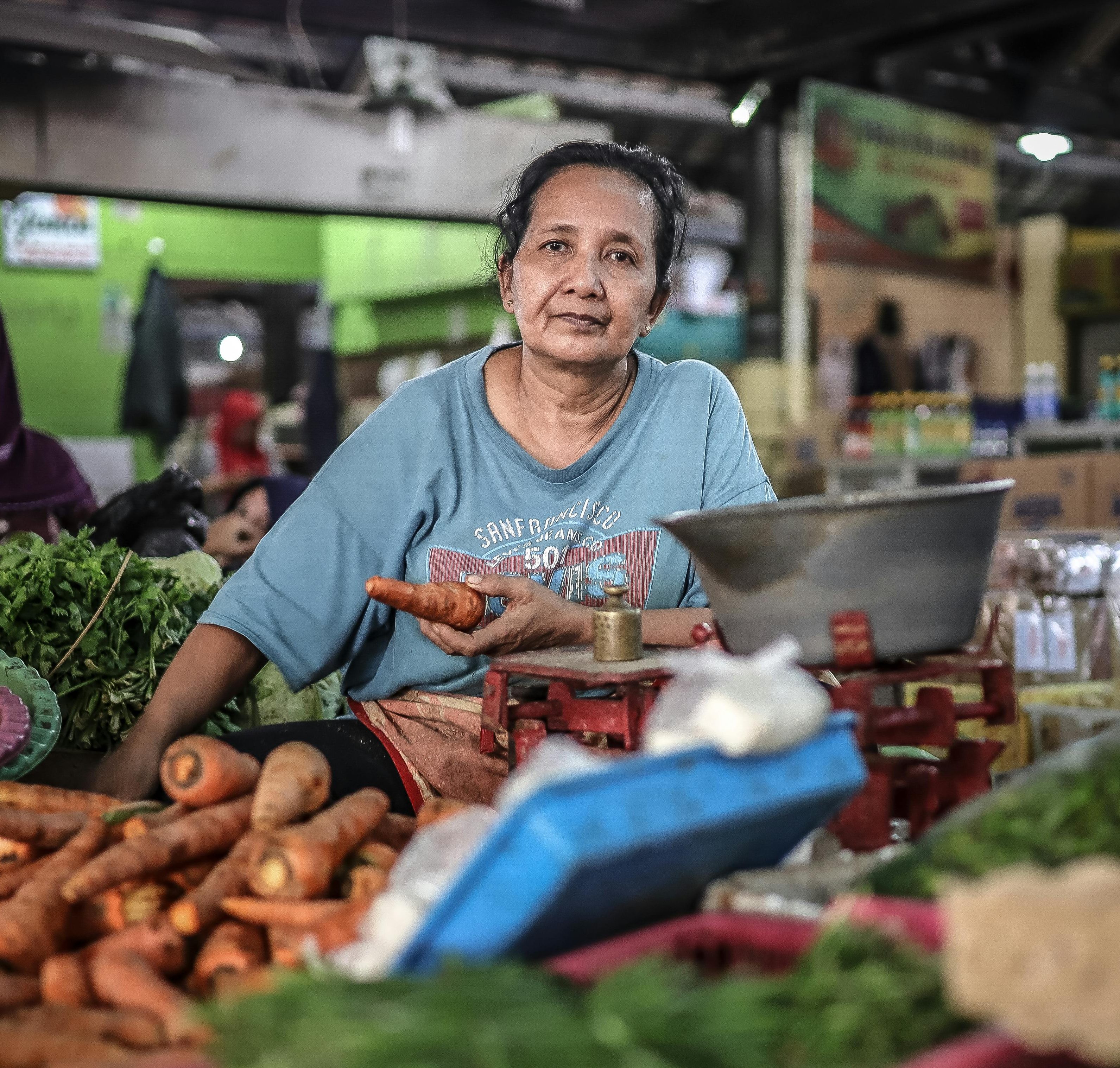 Local woman selling fresh vegetables at an Indonesian market. Vibrant scene with carrots and greens.